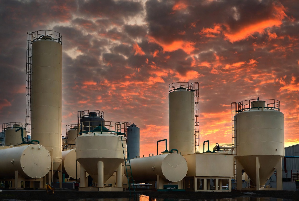 Large-scale industrial GRP/FRP vertical and horizontal storage tanks installed at a chemical processing plant under a dramatic sunset sky