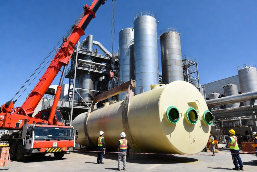 Heavy-duty industrial crane installing a massive FRP chemical storage tank at a large-scale fertilizer processing plant by Global Fiberglass Company.